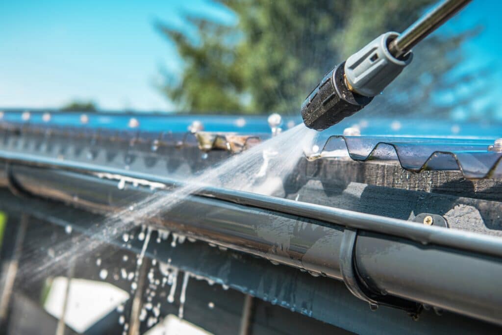 Spring Rain Gutters Cleaning Using Pressure Washer. Closeup Photo. Remove Tiger Stripes